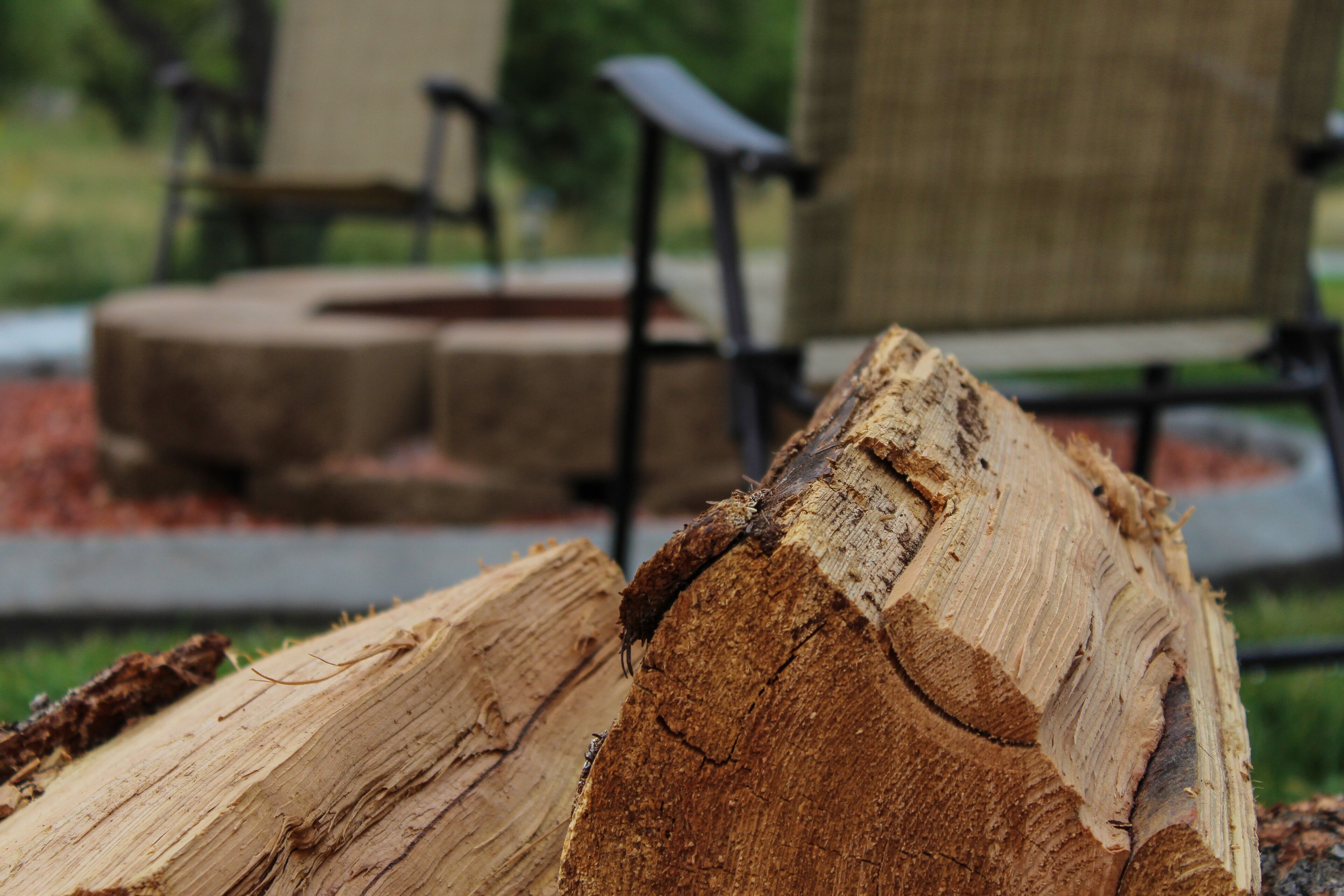 A close-up of a cut log with a rough texture, set against a blurred background of outdoor furniture and a garden area.