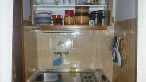 Eine kompakte Küche mit Spüle, Herd und kleinem Kühlschrank. Über der Spüle befindet sich ein Regal mit verschiedenen Küchenutensilien.