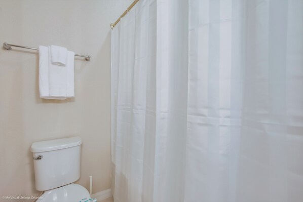 A bathroom with a toilet, a towel rack with a towel, and a shower curtain.
