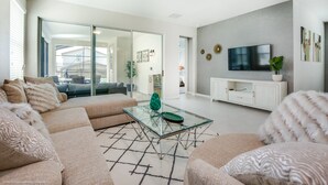 Un salon moderne avec une table basse en verre, des canapés de couleur beige et un téléviseur à écran plat posé sur un meuble blanc.