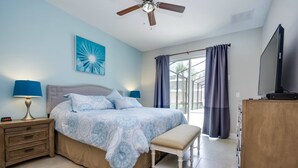 A bedroom with a bed, nightstands, a bench, a ceiling fan, a TV, and a window with curtains. - Solterra Executive Villa 5294 (Davenport)