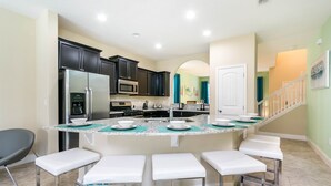 A modern kitchen with dark cabinets, stainless steel appliances, and a central island with bar stools. - Solterra Executive Villa 5287 (Davenport)