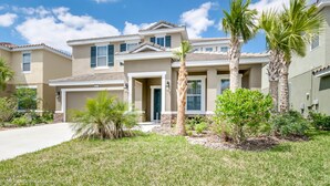 A two-story house with a front garage, a driveway, and a well-maintained lawn with palm trees and shrubs. - Solterra Executive Villa 5287 (Davenport)