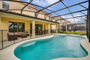 Una piscina con un porche techado, mobiliario exterior y vista a una casa al fondo.