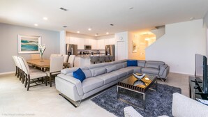 A modern living room with a sectional sofa, a dining area with a table and chairs, a kitchen in the background, and a staircase leading to another level. - Solterra Exec Villas- 6108bod (Davenport)