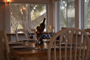 Une table à manger dressée avec des assiettes, des couverts et des verres à vin, une bouteille de vin et une statuette posés sur la table.