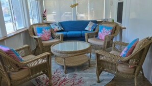 Ein sonnendurchfluteter Raum mit Korbmöbeln, einem blauen Sofa und einem Glastisch.