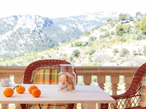A table with a glass jar of seashells and three oranges, a cup, and a saucer, set on a balcony with a mountain view. - Can Cega - Beautiful house with terrace and views in Bunyola (Bunyola)