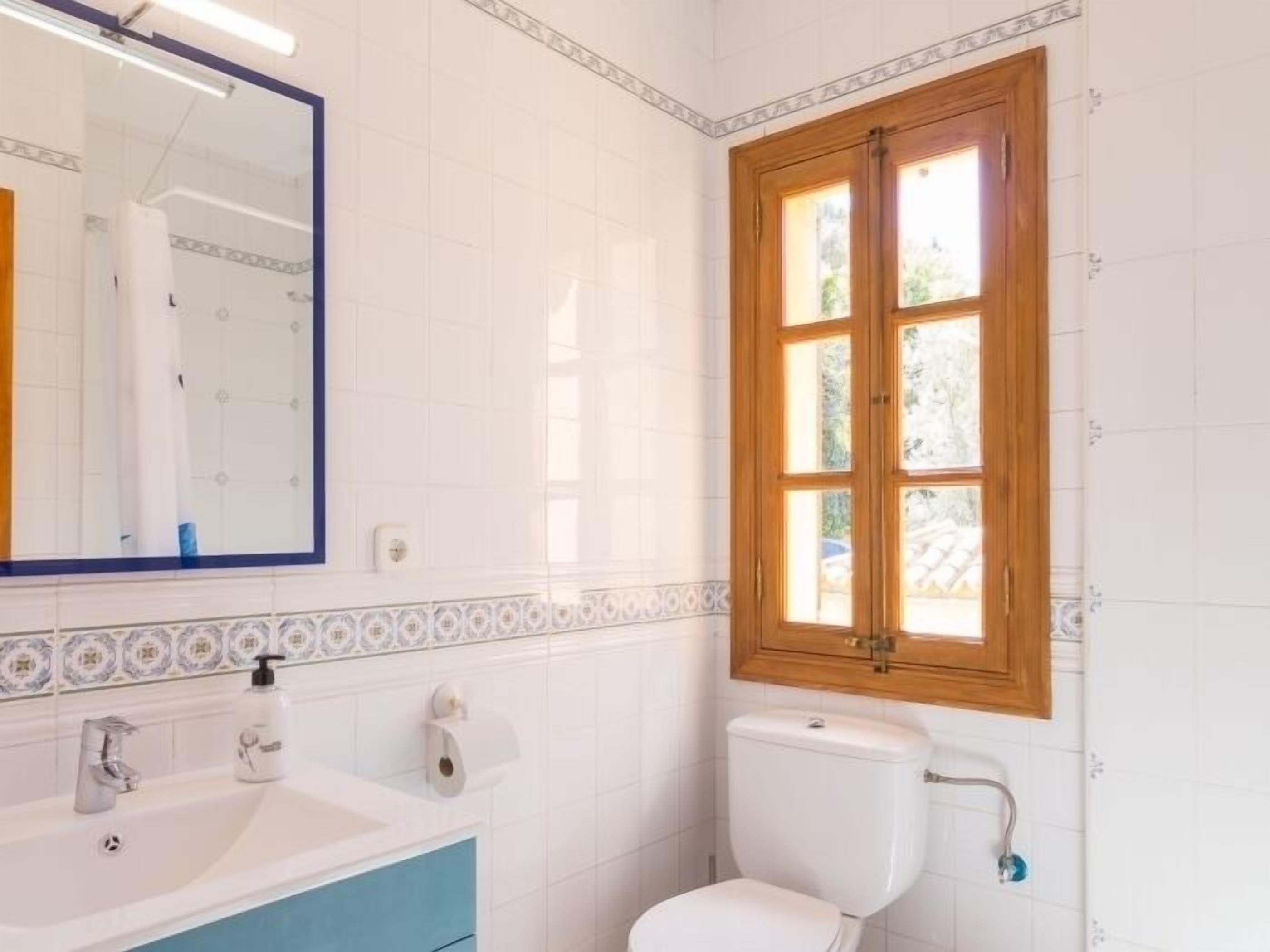 A bathroom with a white sink, a mirror, a toilet, and a window with wooden frames.