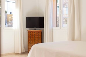 A bedroom with a bed, a wooden dresser, a television, and a window with curtains.