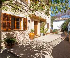 Une cour intérieure avec un bâtiment doté de volets en bois, de plantes en pot et d’un escalier en pierre.