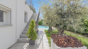Un edificio moderno con una escalera que lleva a un área de piscina rodeada de follaje y un árbol.