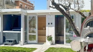 Una casa moderna con puerta de cristal, un pequeño patio con mesa y sillas, y un árbol en primer plano.
