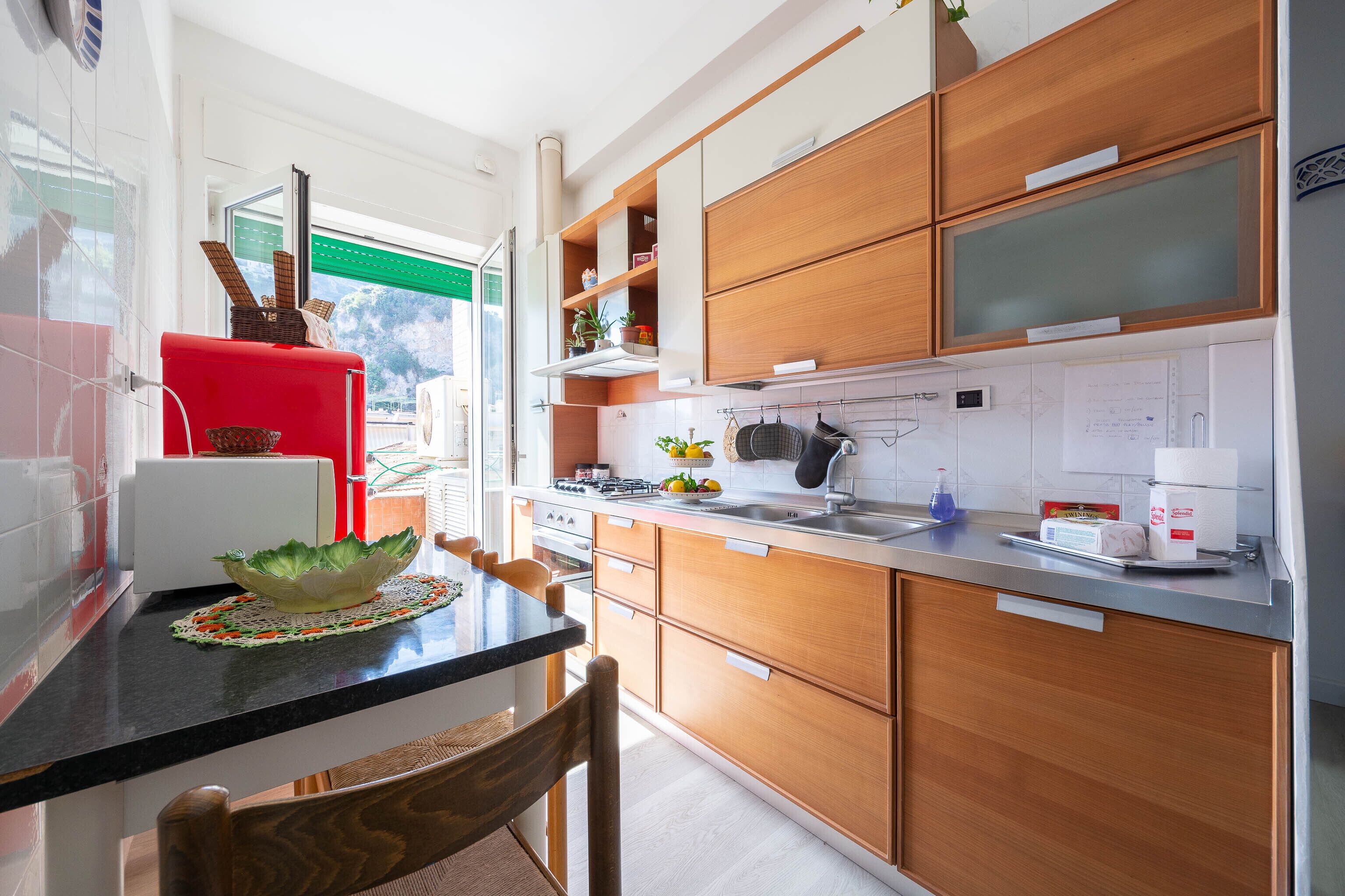A modern kitchen with wooden cabinets, a black countertop, and a red appliance.