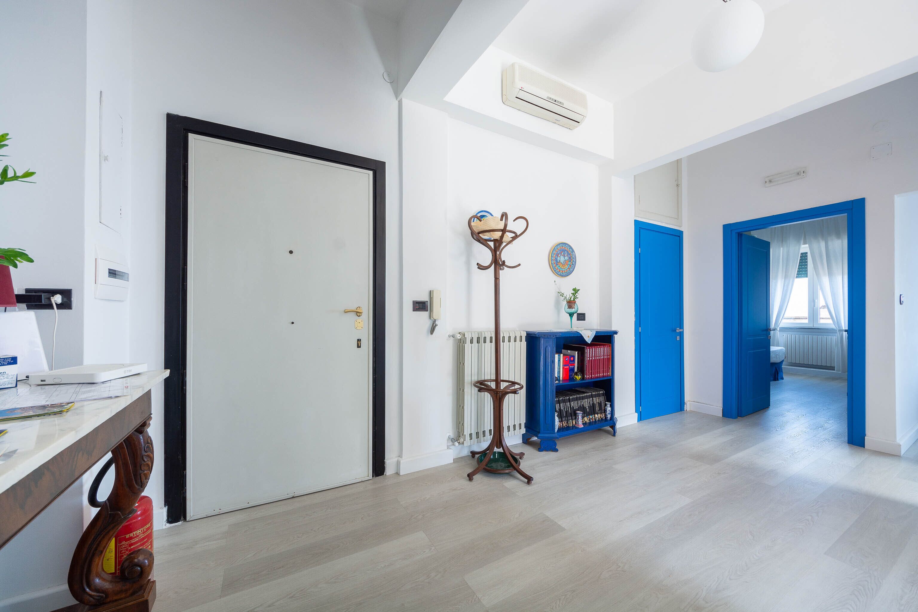 A hallway with a white door, a radiator, a blue bookshelf, and a coat stand.