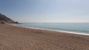 A beach with a clear sky, a sandy shore, and a few people in the distance. - Casa Roberta (Maiori)