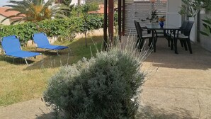 A covered patio area with a table and chairs, surrounded by greenery and a small bush. - Apartment in Mali Lošinj with Balcony, Air condition, WIFI (72-1) (Mali Lošinj)