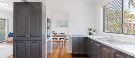 Una cocina moderna con armarios oscuros, piso de madera y un ventanal con vistas a palmeras.