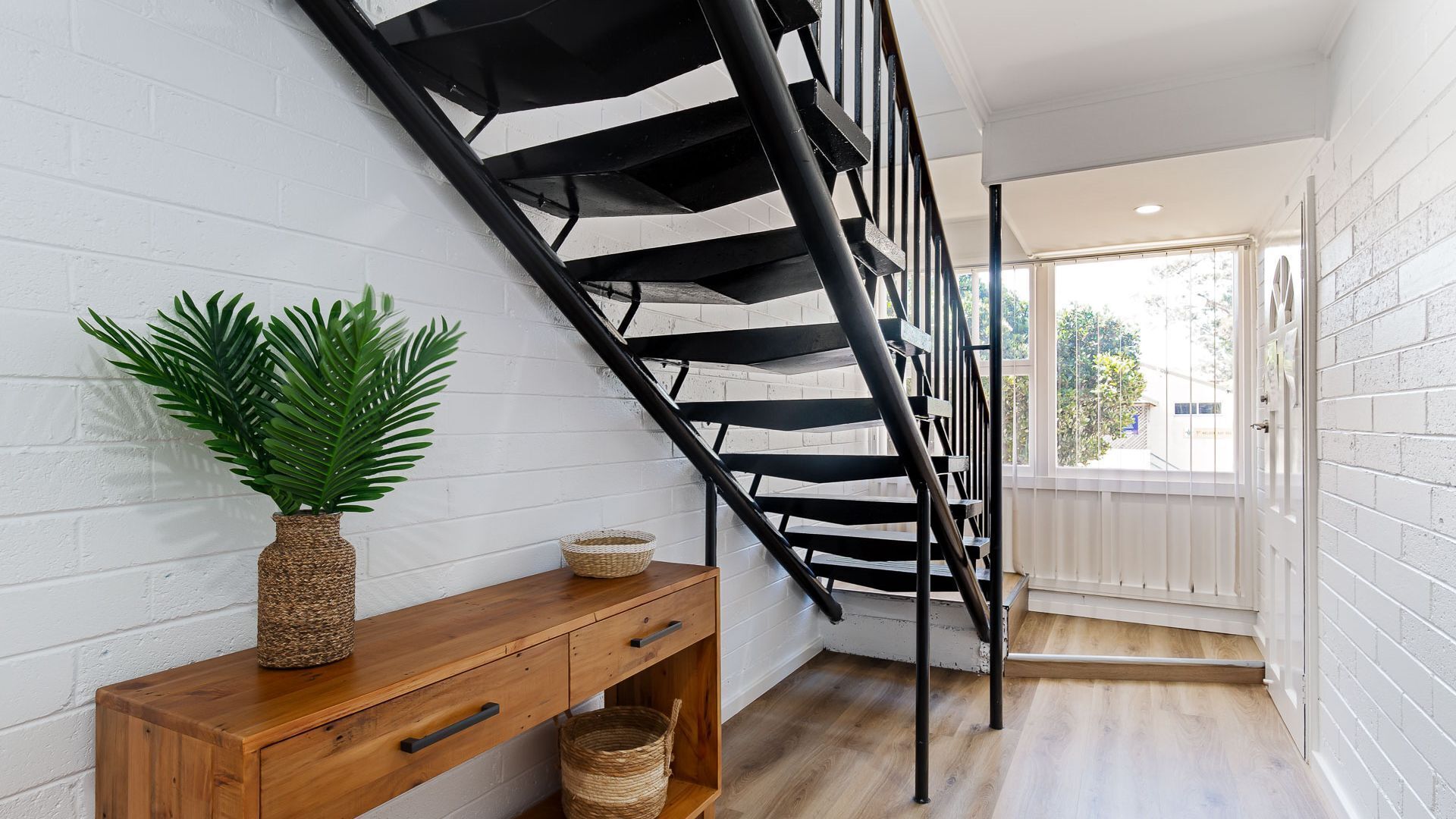 A staircase with black railings, a wooden console table with baskets, and a potted plant.