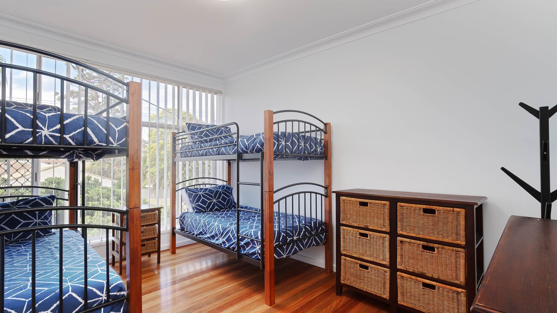 A bunk bed room with a view of the outdoors, a wooden dresser, and wicker baskets.