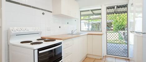 A modern kitchen with white cabinetry, a built-in oven, a stove, and a window overlooking a garden.