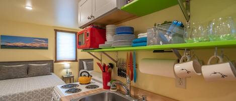 Cocina compacta con lavamanos, estufa y una cama en la habitación contigua.
