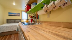 A small kitchenette with a wooden countertop, a sink, and a shelf with cups and plates. - Cabin 5 · Emigrant Cabins #5 - Affordable Tiny Cabin in MT (Emigrant)