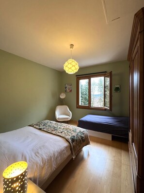 A bedroom with a bed, a chair, a window, and a lamp.