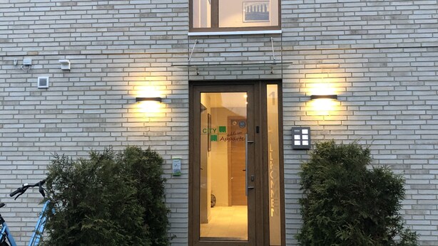 Un edificio moderno con fachada de ladrillo, puerta de vidrio de entrada y dos pequeños arbustos en la parte frontal.