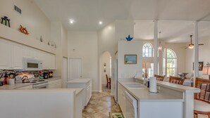 A spacious kitchen with white cabinetry, a central island, and a dining area with wicker chairs. - Long Water View, Pool, Kayaks, Bikes, Views,116 Reviews! Villa 21 (Cape Coral)