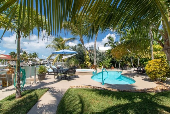 A pool area with a table and chairs, surrounded by palm trees and a clear blue sky.