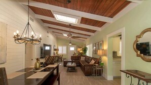 A spacious living room with a wooden ceiling, a dining area with a table and chairs, and a cozy seating area with a sofa and armchairs.
