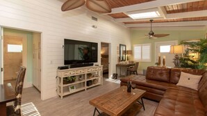 A spacious living room with a large TV, wooden ceiling, and a brown leather sofa.