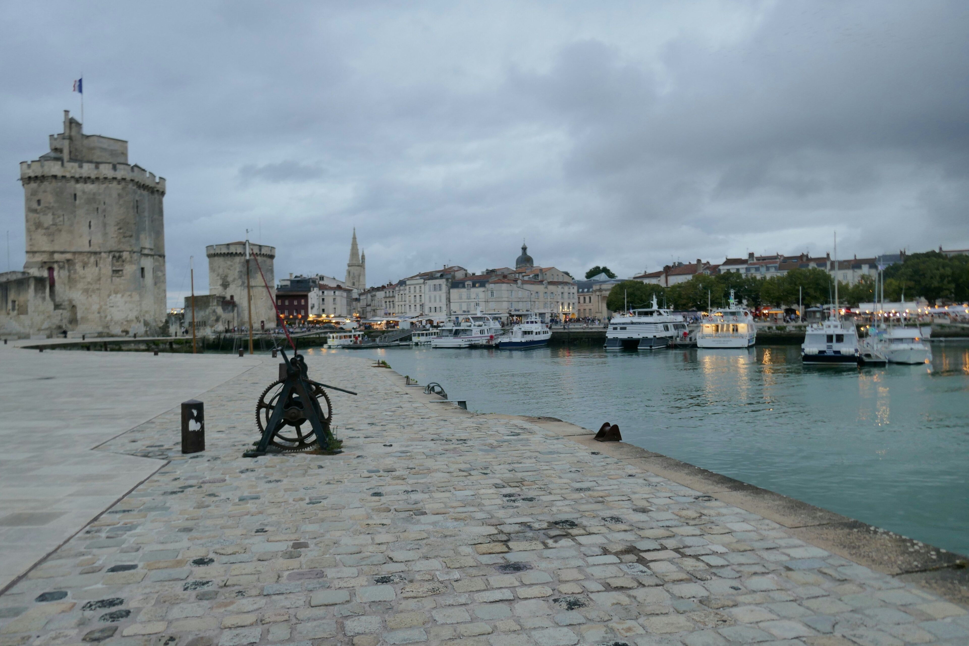 Une promenade en bord de mer, avec une tour historique, des bateaux amarrés et un sentier pavé.