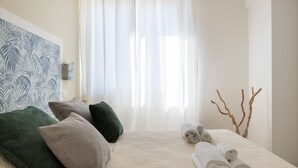 Ein ordentlich bezogenes Bett mit aufgerollten Handtüchern, einem grün-grauen Kopfkissen und einem dekorativen Zweig am Rand.