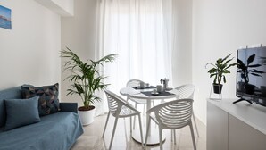 Ein modernes Wohnzimmer mit einer Couch, einem Esstisch mit Stühlen, einer Topfpflanze und einem Fernseher auf einem Beistelltisch.