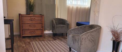 A living room with a sofa, a chair, a wooden dresser, and a window with curtains.