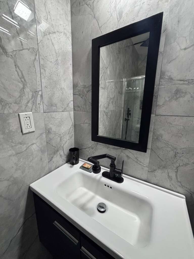 A bathroom with a white sink, black faucet, and a mirror with a black frame.
