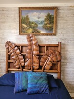 Una cama con cabecera de madera con diseños de hojas, un cuadro de un paisaje en la parte superior y dos almohadas sobre la cama.