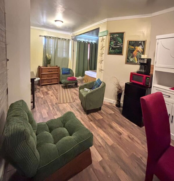 A living room with a green sofa, a red chair, a wooden cabinet, and a microwave. - Cocoplum Rest N Hideaway 1 (Nassau)
