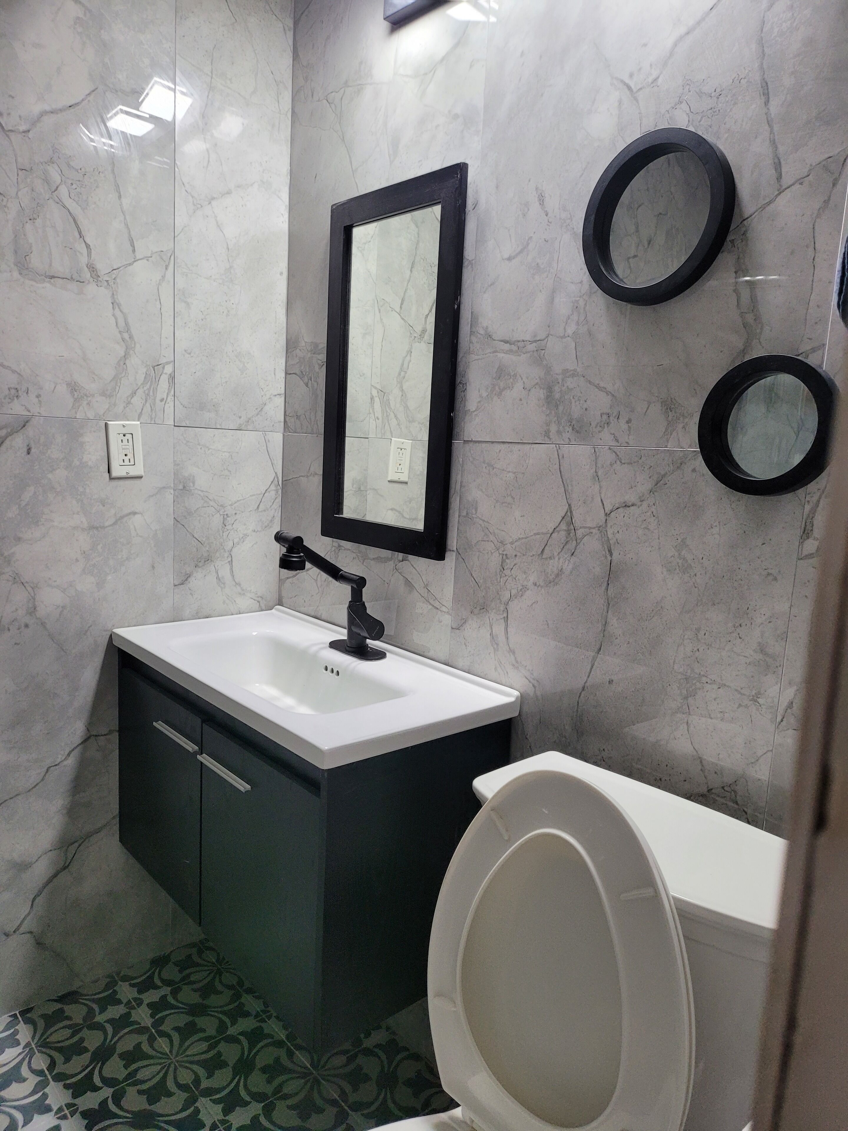 A bathroom with a white sink, black cabinet, and a toilet. There are two mirrors on the wall.