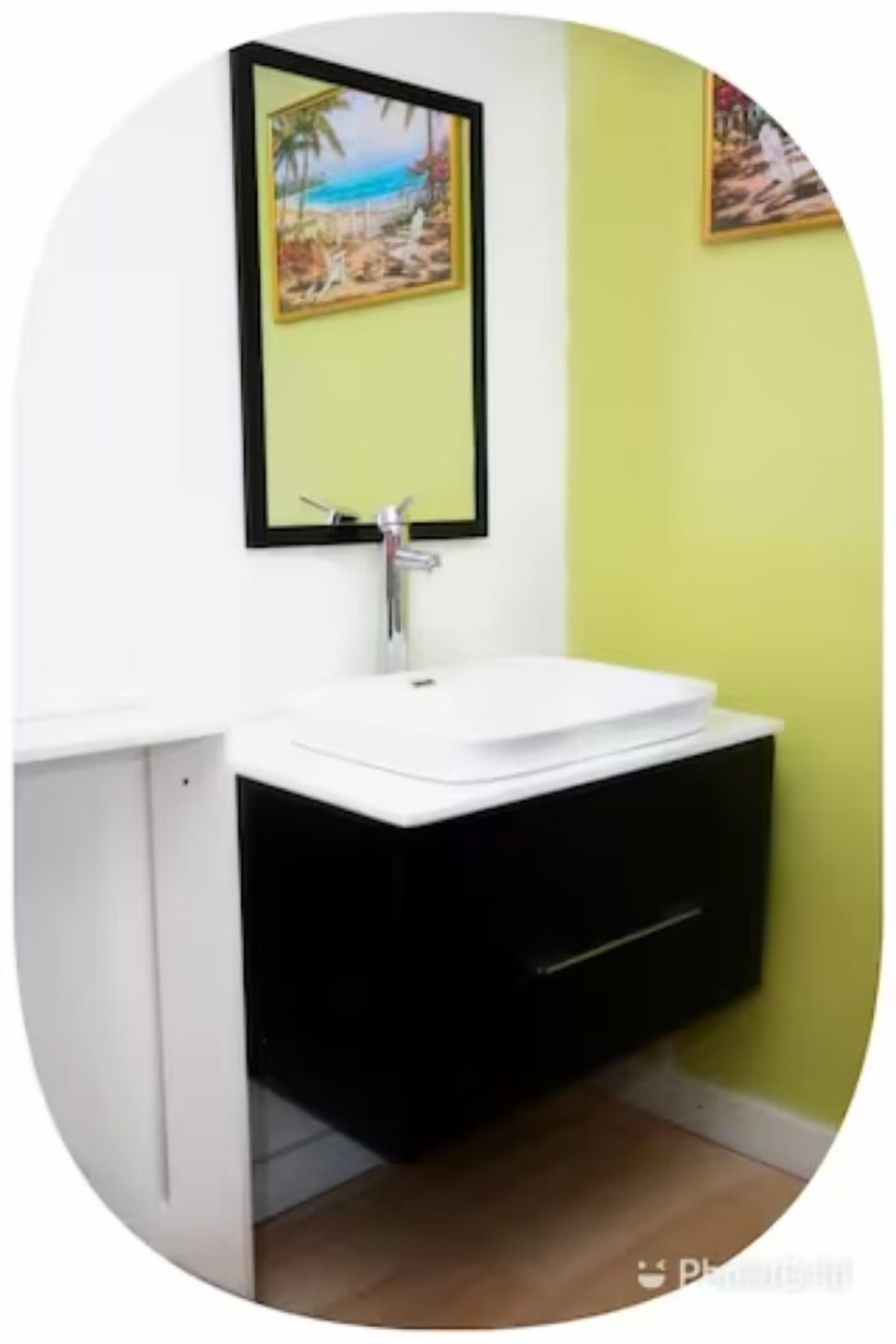 A bathroom with a white sink, black cabinet, and a painting of a beach scene on the wall.