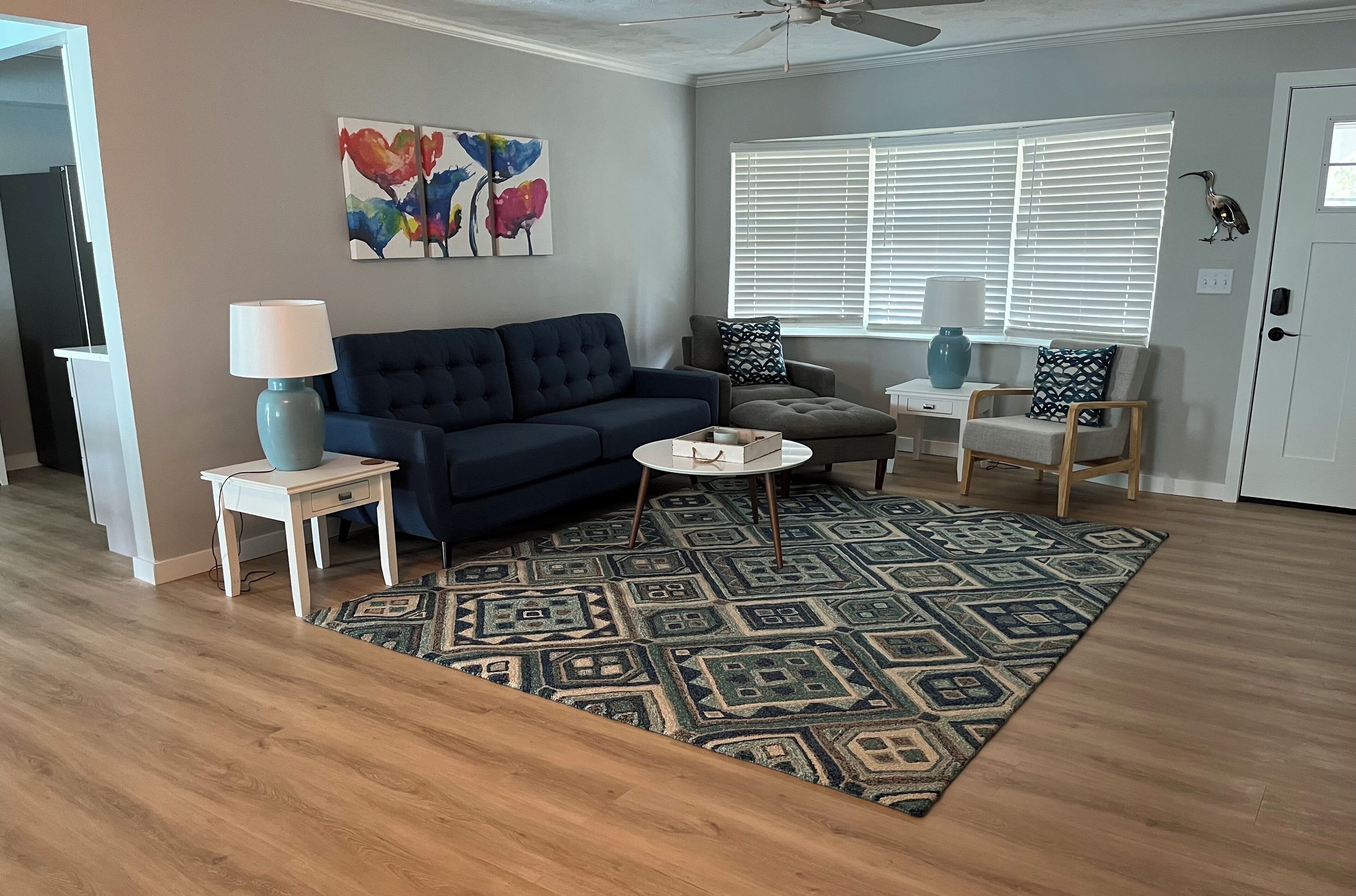 A living room with a blue sofa, a patterned rug, a lamp, and a window with blinds.