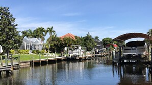 Um canal com barcos atracados à direita, uma ponte coberta e uma casa com telhado vermelho ao fundo.
