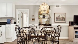 A dining area with a glass-top table, metal chairs, and a pendant light. - Experience Lighthouse Point 35C– Your North End Tybee Retreat (Tybee Island)