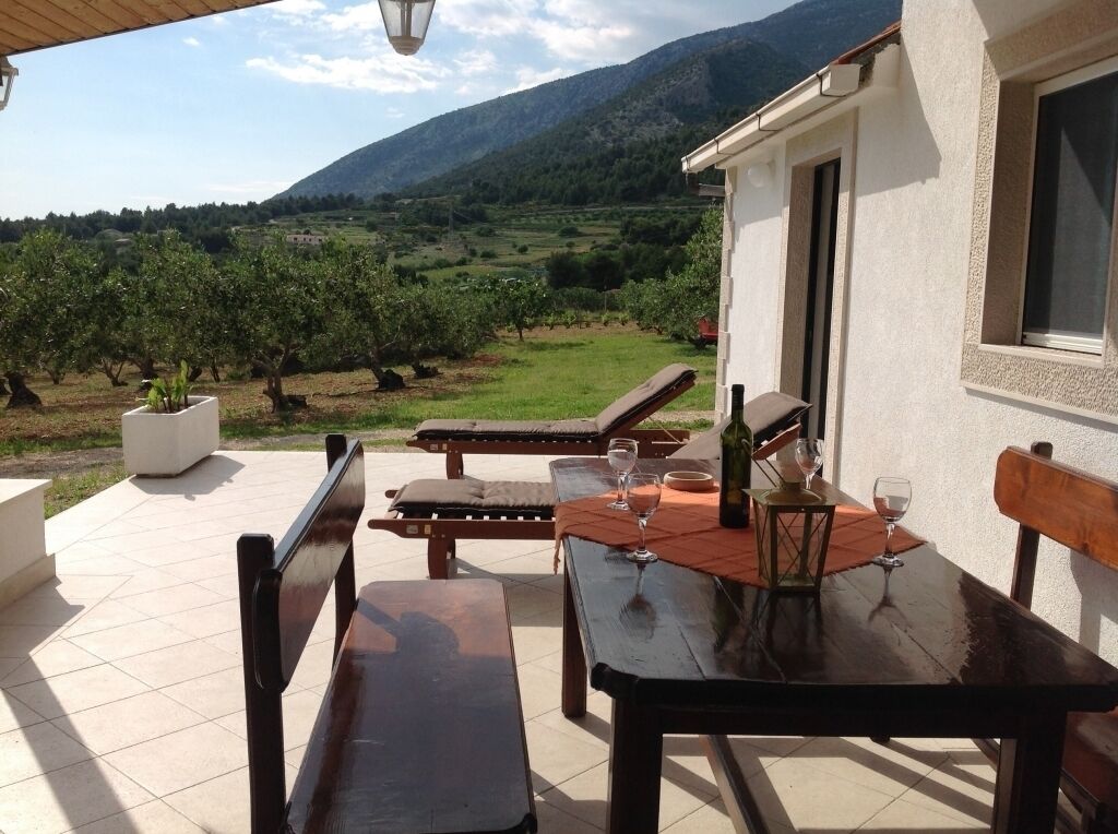 Eine Außenpatio mit Tisch und Stühlen, einem Topfpflanzen und Blick auf einen Weinberg und Berge.