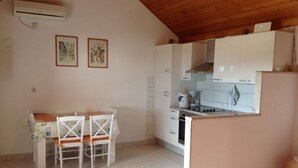 Une cuisine compacte avec des meubles blancs, un coin repas comprenant une table et des chaises, et un petit îlot central.