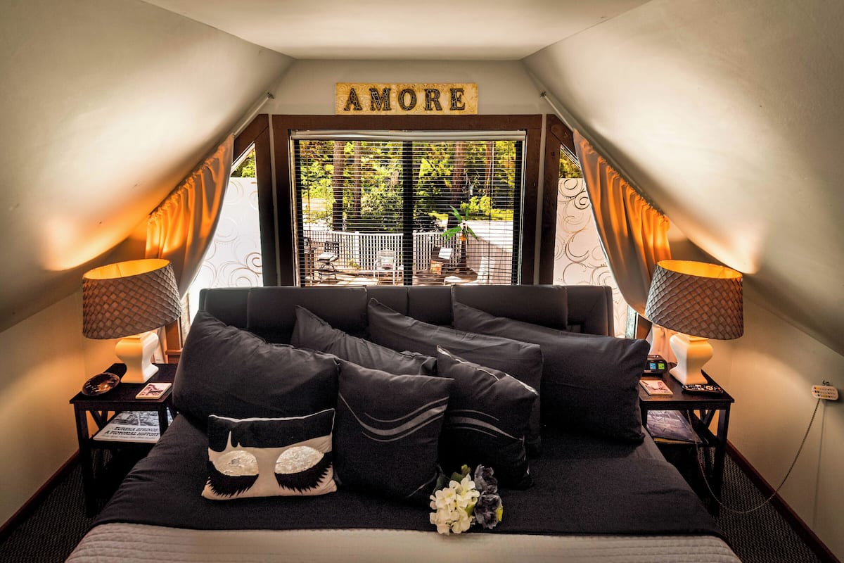 A bedroom with a large bed, two bedside tables, a window with curtains, and a sign above the window that reads "AMORE".