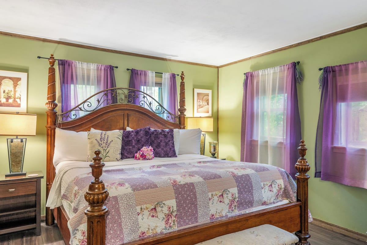 A neatly made bed with a floral quilt, a wooden headboard, and a footboard. There are two bedside tables with lamps and a framed picture on the wall.