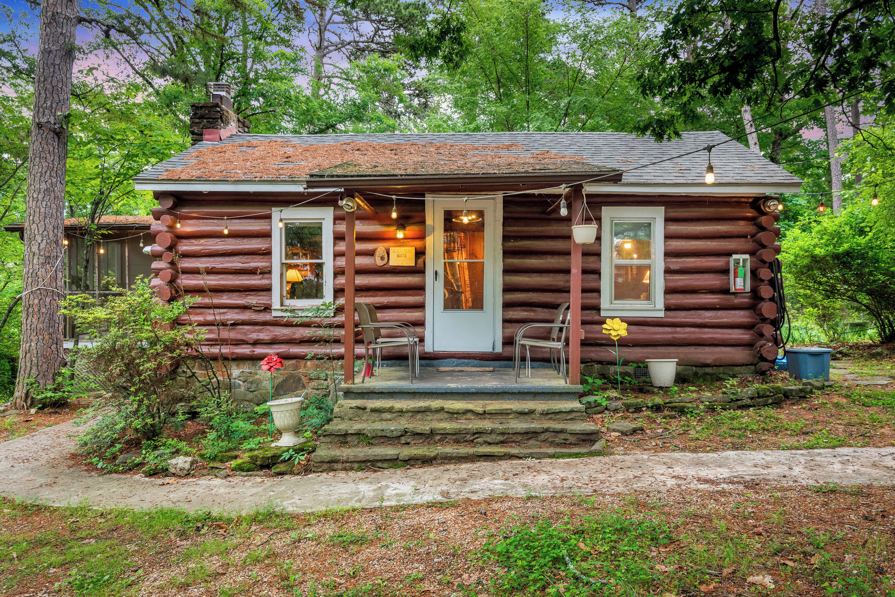 Une cabane rustique en rondins de bois, dotée d’une véranda, de deux chaises et d’un pot de fleurs.